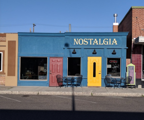 A colorful storefront labeled "NOSTALGIA" with blue walls, a yellow door, and outdoor seating.